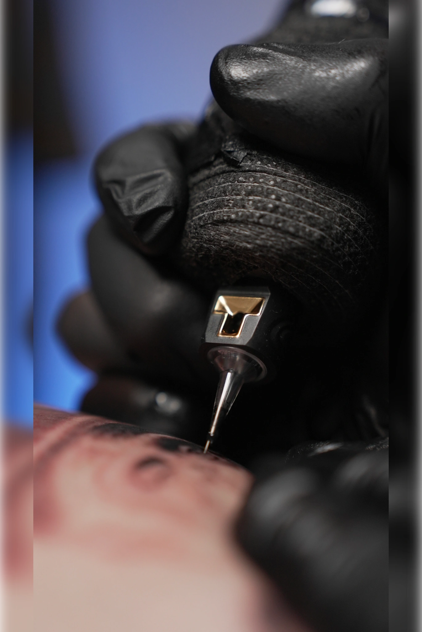 Zbliżenie dłoni w&nbsp;rękawiczce i&nbsp;maszynki podczas tatuowania